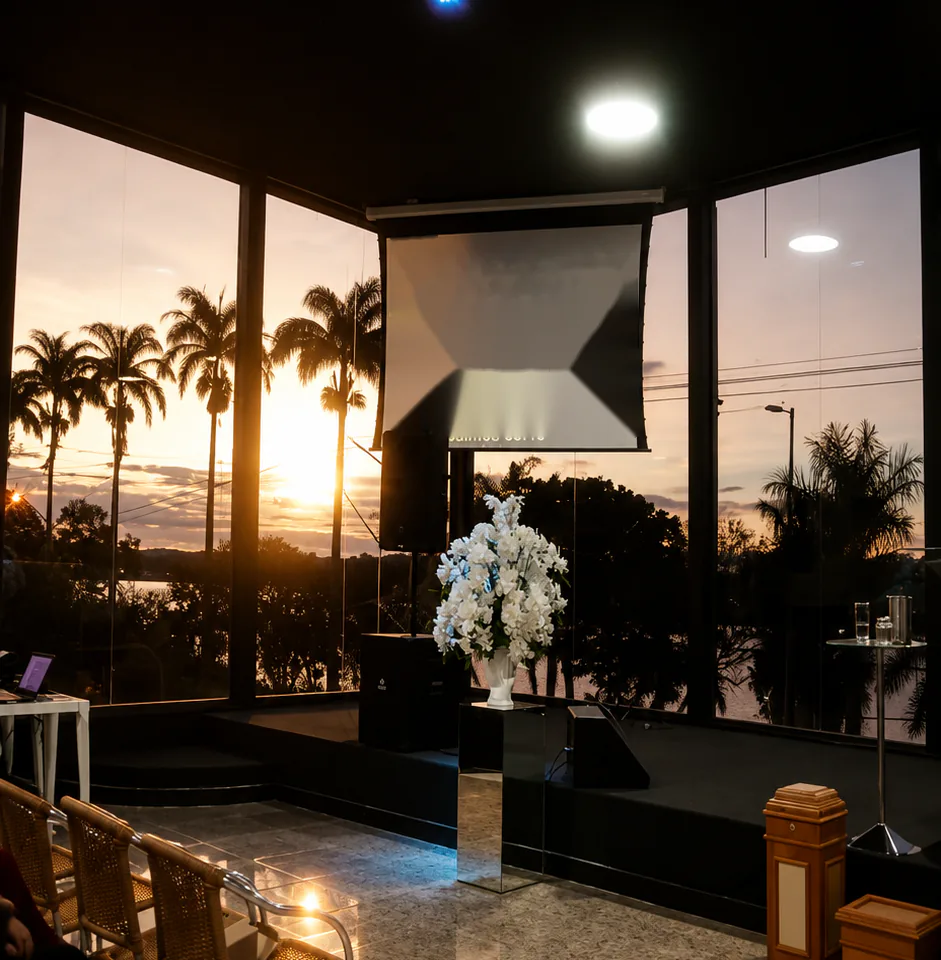 Palco ao pôr do sol, com o telão e flores brancas diante das janelas para a lagoa